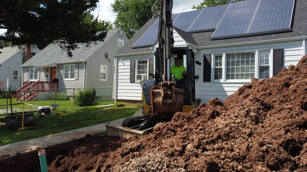 Excavator beside a home during an outdoor plumbing excavation project