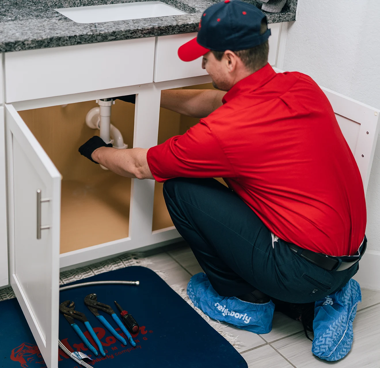 Mr. Rooter plumber inspecting accessible plumbing beneath a sink while wearing shoe covers